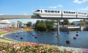 A monorail crosses over a lake lined with colorful flowers.